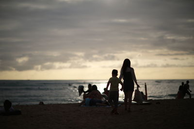 Silhouette people at beach against sky during sunset