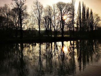 Silhouette bare trees by lake against sky during sunset