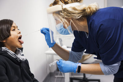 Female doctor performing covid-19 swab test on boy patient