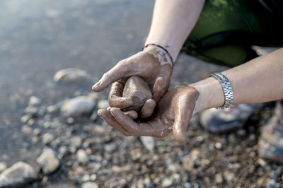 Woman with muddy hands holding a stone outdoors in nature.