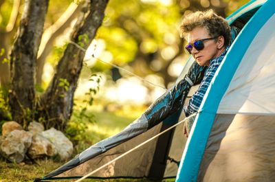 Senior woman looking out of tent at campsite 