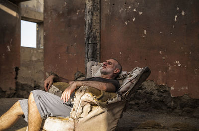 Adult man sitting on an old sofa of an abandoned house