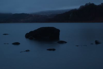 Rocks in lake against sky at dusk