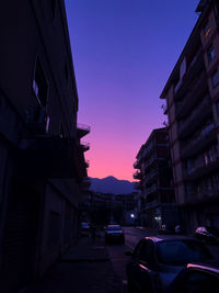 Cars on street amidst buildings against sky at sunset