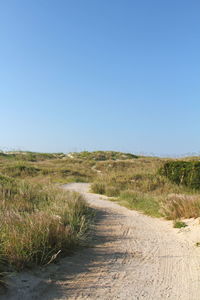 Dirt road in field against clear blue sky