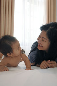 Mom is playing with a baby under 2 years old on a white-sheeted bed