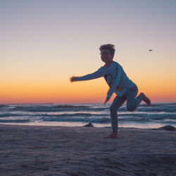 Full length of man on beach against sky during sunset