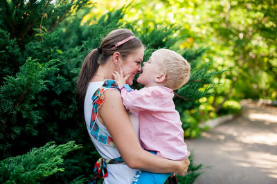 Happy mother and daughter standing against trees