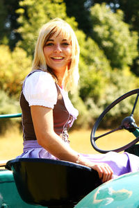 Portrait of young woman wearing dirndl while sitting on tractor