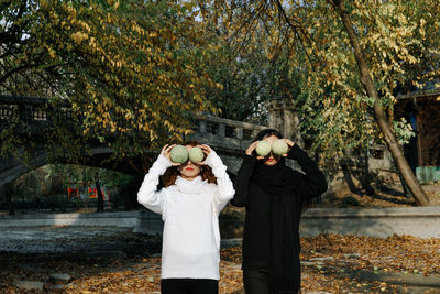 Lesbian couple holding fruits while standing against trees in park during autumn