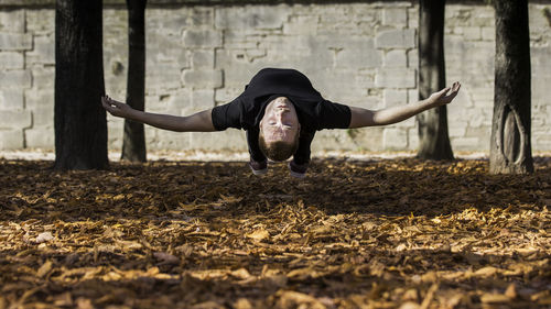 Young man with arms outstretched levitating over dry leaves