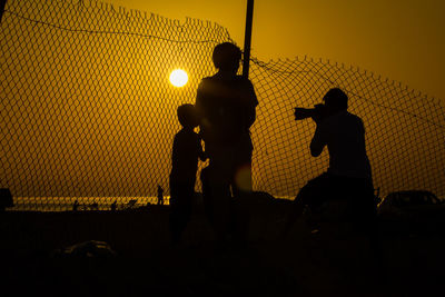 Silhouette men standing against orange sky