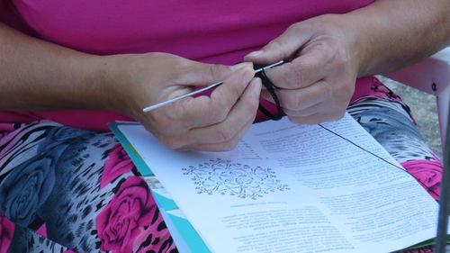 Midsection of woman with design book crocheting on chair