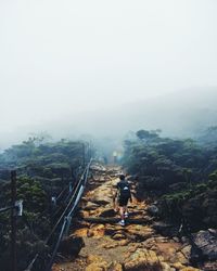 Rear view of woman walking on mountain against sky during foggy weather