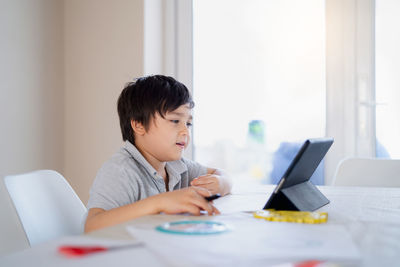 Rear view of boy sitting on table at home