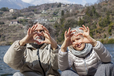 Beautiful mature couple showing symbol of the heart with hands on the dock on a winter day