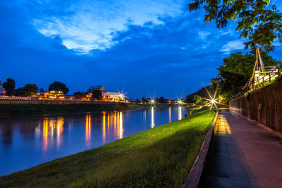 Illuminated city by river against sky at dusk