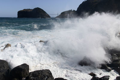 Waves splashing on rocks at shore against sky