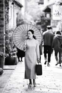 Full length of woman holding umbrella while standing on street