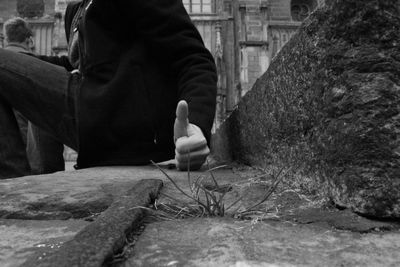 Midsection of man showing thumbs up while sitting on retaining wall