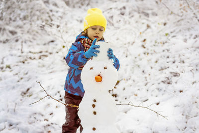 Boy in warm clothing making a snowman.