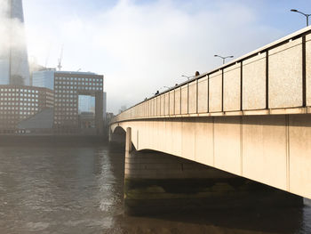 Bridge over river by buildings against sky