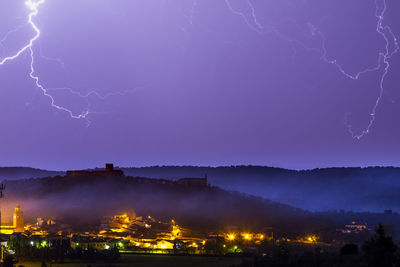 Lightning over illuminated city against sky at night