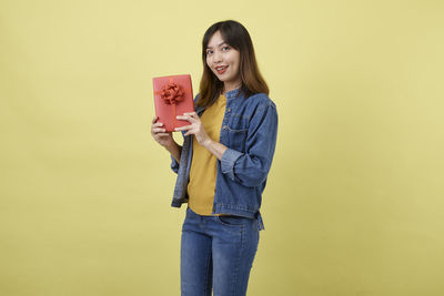 Portrait of smiling young woman standing against yellow background