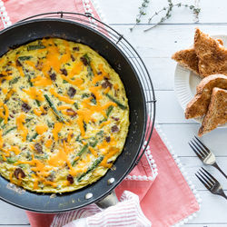 An asparagus and bacon frittata topped with melted cheese, ready for serving.