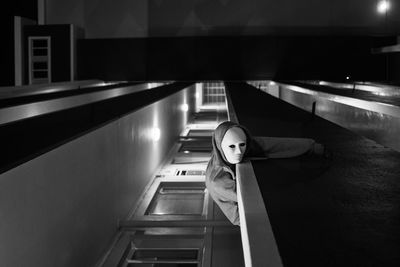 Tilt image of person wearing mask while bending in balcony at night