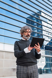 Mature handsome business man using a digital tablet outside office building