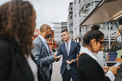 Male and female business professionals waiting for food while standing near food truck