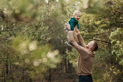 Side view of father and son standing against tree