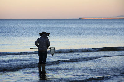 Rear view of silhouette man standing at beach against sky