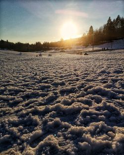 Surface level of snow covered land against sky during sunset