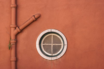 Close-up of circle window by pipe on wall