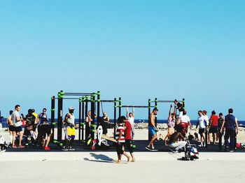 People at beach against clear blue sky