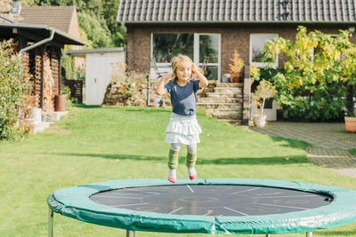 Full length of girl playing on trampoline in yard