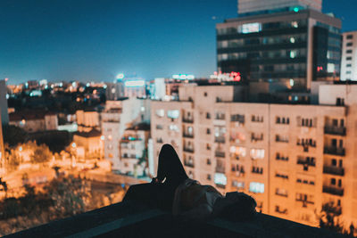 Low section of person against illuminated buildings in city at night