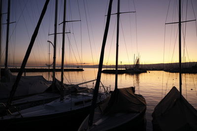 Sailboats moored in sea at sunset