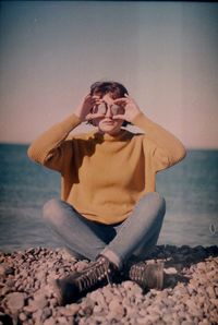 Young woman sitting on beach against clear sky