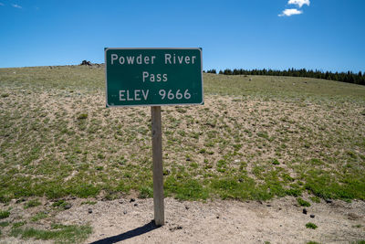 Information sign on field by road against sky