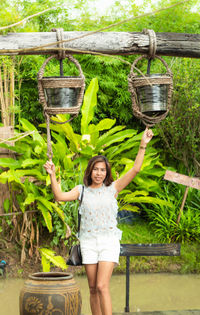 Portrait of woman standing under buckets against plants