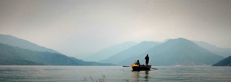 Silhouette people on boat sailing in river against sky