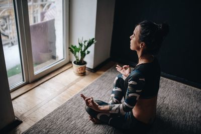 Side view of woman doing yoga while sitting at home