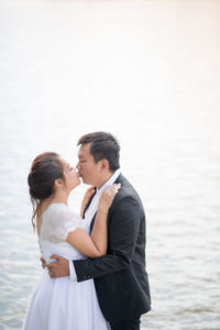 Side view of newlywed couple kissing while standing against sea