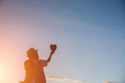 Silhouette man holding orange against sky during sunset