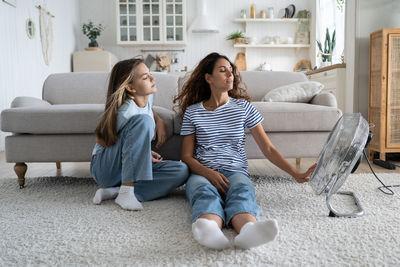 Loving carefree woman mom and teenage girl sits in relaxed position on floor in living room near fan