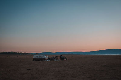 People and van by tents at campsite against sky during sunset