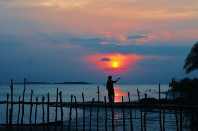 Silhouette people standing by sea against sky during sunset